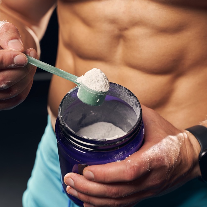 shirtless-muscly-man-wearing-sport-shorts-scooping-powder-protein-from-jar