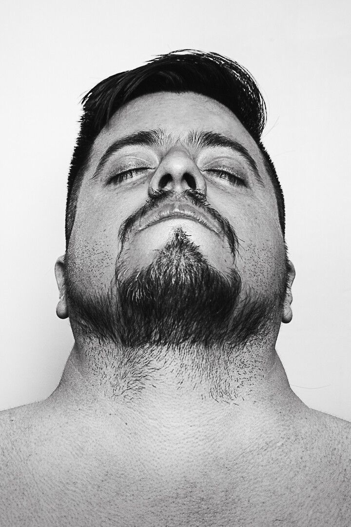 Autorretrato en blanco y negro de un hombre con barba visto desde un ángulo bajo, resaltando sus rasgos faciales y expresión seria.