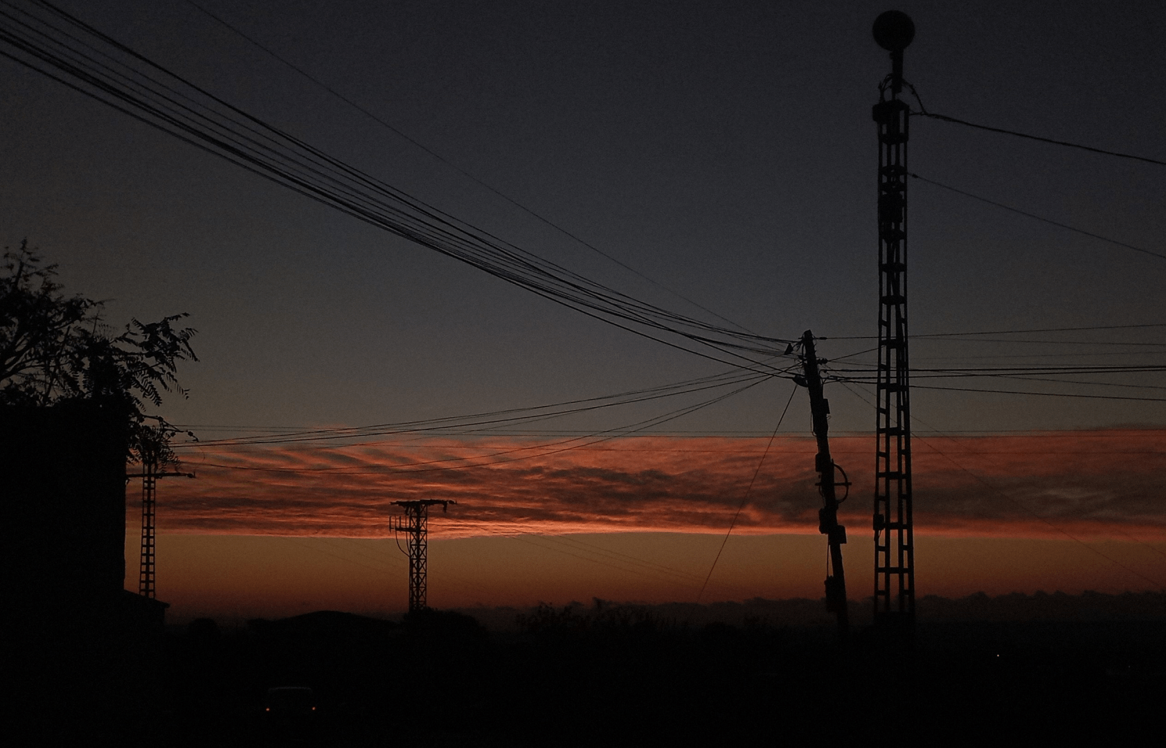 Amanecer. Se ve una franja oscura bajo el horizonte, la silueta de un muro coronado por plantas a la izquierda y dos postes a la derecha. Del más bajo parten cables que van hacia arriba, a la izquierda. Sobre el horizonte, una estrecha franja de colores azul y naranja oscuros. Por encima de esa franja una nube estrecha que atraviesa el cuello, la parte inferior de la nube muestra una franja naranja brillante que anuncia la cercanía del sol, con el que ya está hablando. Luego viene la oscuridad y por las parte superior de la nube otra franja brillante, más borrosa. Por encima de la nube se ve el cuello que en la parte inferior comienza a ser azul y se sienta en la oscuridad según se aleja del punto del amanecer.