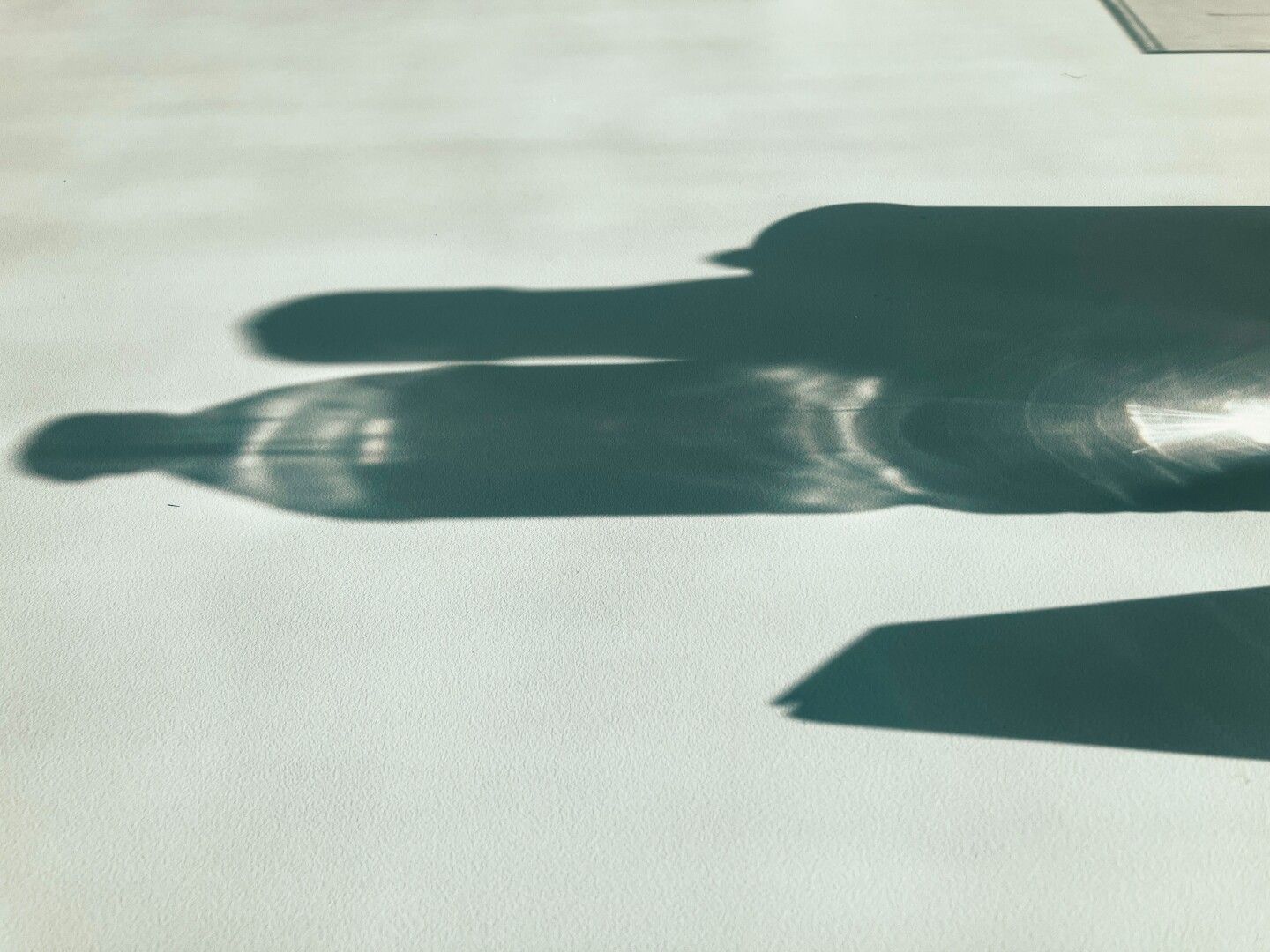 Sombras de una botella de agua y un objeto sobre una mesa blanca.