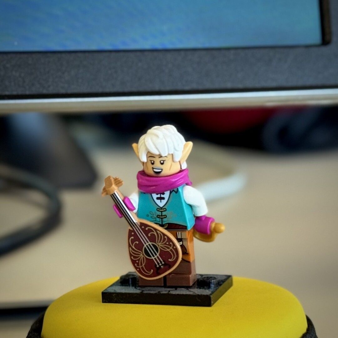 Minifigura de Lego de Bardo elfo con pelo blanco, orejas picudas, chaleco aguamarina, instrumento musical en una mano y cuchillo en la otra.